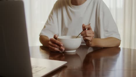 woman eating breakfast while working on laptop