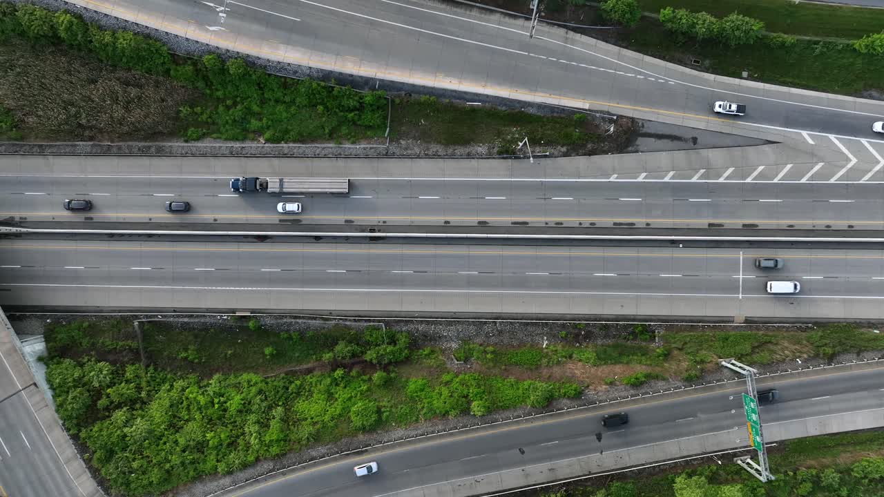 Traffic scene with cars and Trucks on american interstate and highway. Overpass and underpass roads between green trees in spring. Aerial top down flyover shot.
