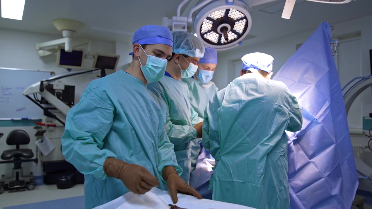 Equipe medica maschile che indossa uniformi blu lavora in sala operatoria. Il giovane assistente passa gli strumenti ai chirurghi che operano.