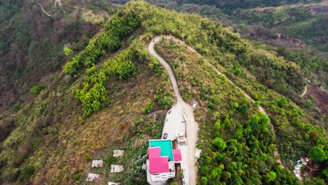 An-aerial-view-capturing-a-solitary-house-on-the-mountains-of-Mizoram,-with-a-vehicle-traversing-on-the-lonely-road