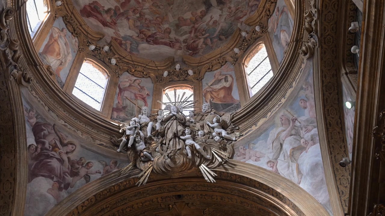 Sculture barocche e affreschi dipinti sul soffitto riempiono l'interno della cupola ornata della Chiesa di San Nicola in una luce soffusa.