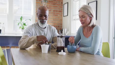 mixed race senior couple talking to each other while having coffee at home