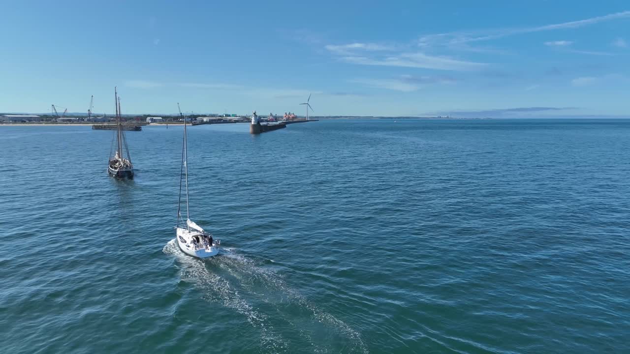 Rotating aerial clip of 2 ships sailing towards industrial harbour with wind farm in the background
