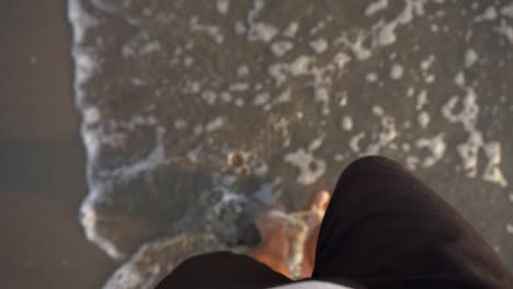 top view of a man walking on sandy beach during sunset.  feet walking on the beach in slow motion.