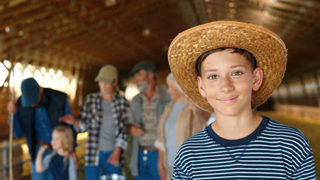 retrato de un adolescente caucásico con sombrero parado en un establo y sonriendo a la cámara