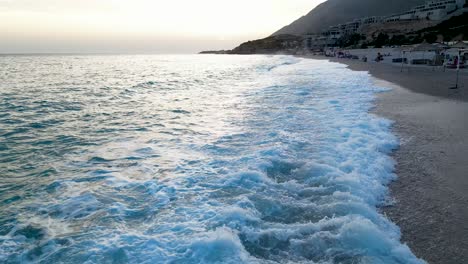 Toma-Aérea-De-Una-Hermosa-Costa-Con-Olas-Rompiendo-En-Una-Playa-De-Arena-Al-Atardecer-En-El-Mediterráneo