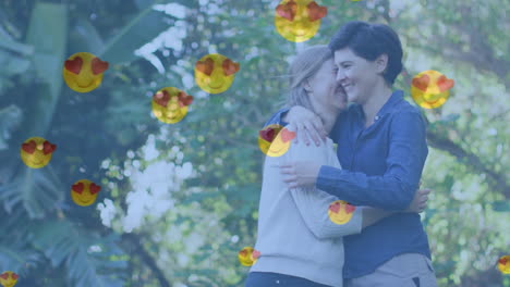 animación de emojis de corazón sobre una feliz pareja de mujeres caucásicas enamoradas abrazándose