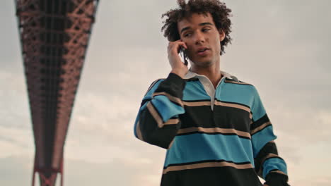 Serious-zoomer-calling-phone-cloudy-day-closeup.-Millennial-guy-talking-mobile