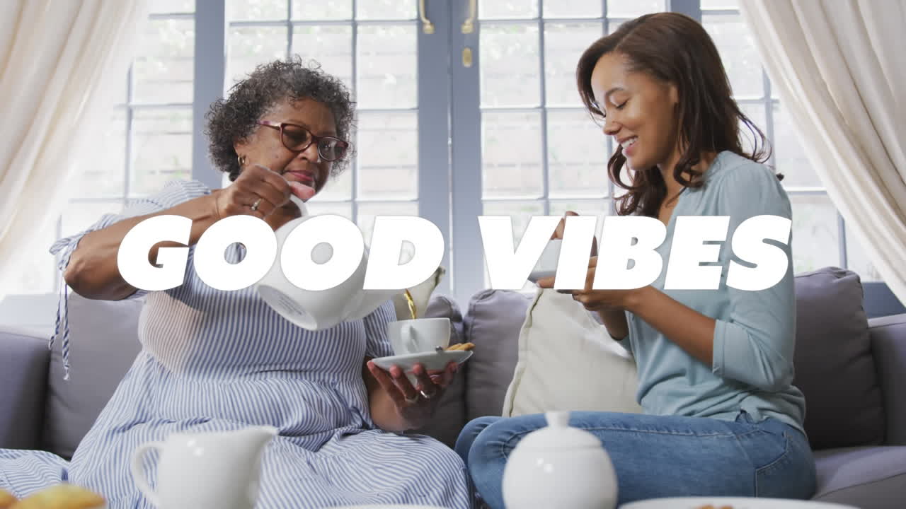 Animation of good vibes text over two women having tea and smiling at home
