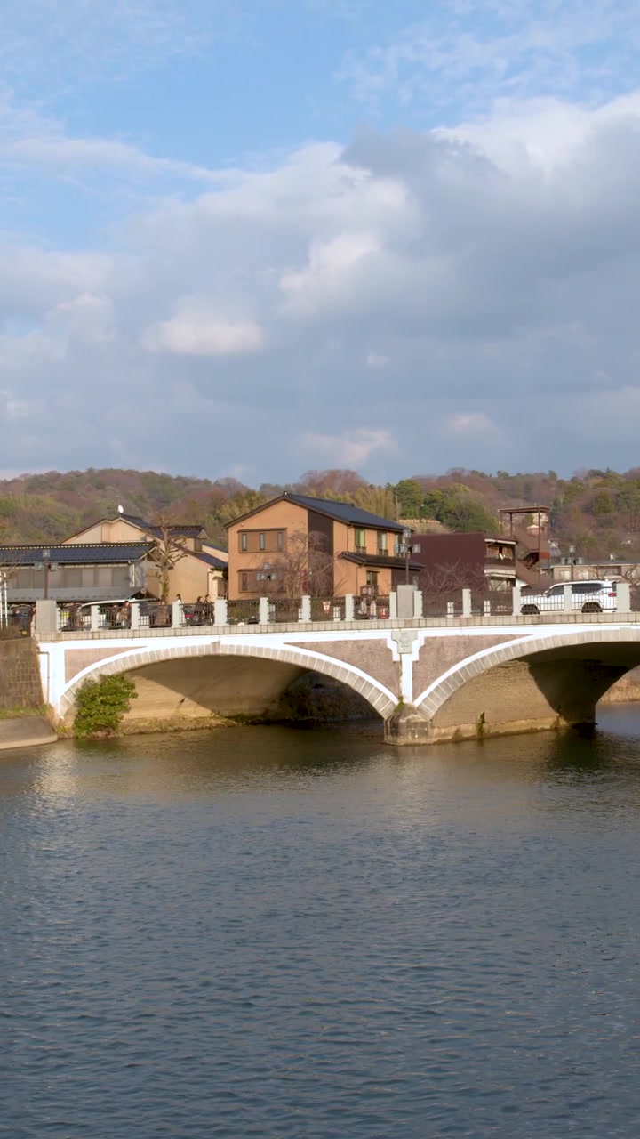 Un'ampia panoramica riprende il ponte storico e l'architettura del lungofiume sotto cieli nuvolosi.