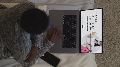 overhead shot of woman lying on bed at home looking at online fashion sale bargains on laptop