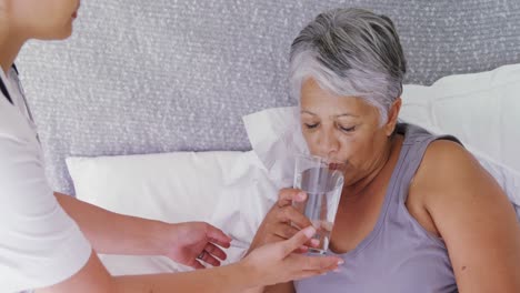 Female-doctor-giving-sick-senior-woman-a-glass-of-water-on-bed-4k