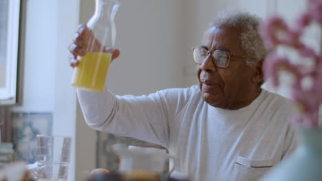 closeup of black senior man pouring orange juice in glass.