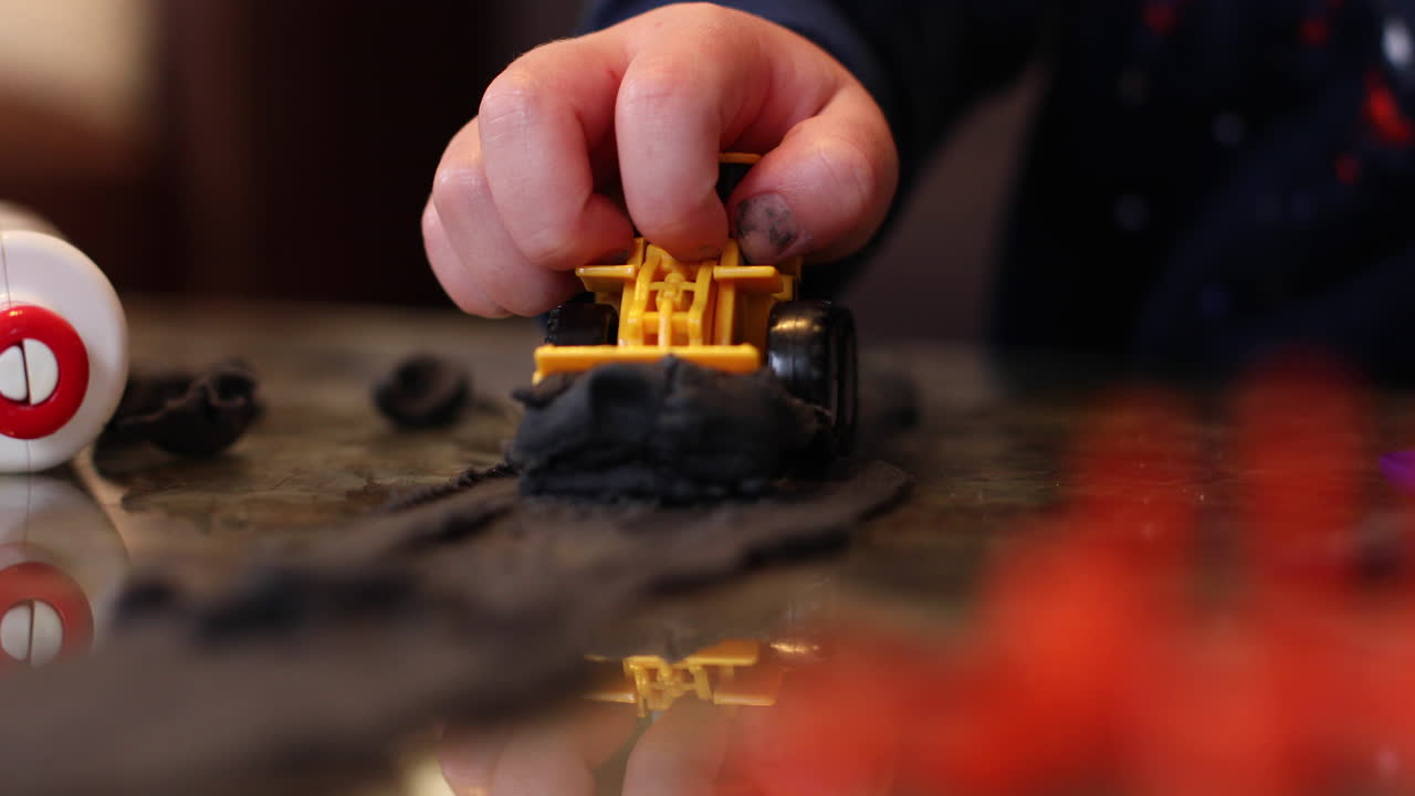 un primer plano de las manos de un niño jugando con su excavadora de remolque y arcilla adentro durante el encierro