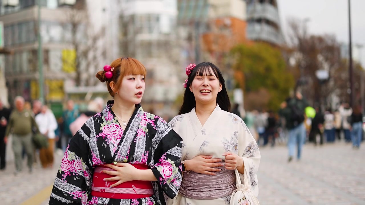 Dua teman yang tersenyum mengenakan yukata tradisional berjalan di jalan Harajuku yang ramai di Tokyo