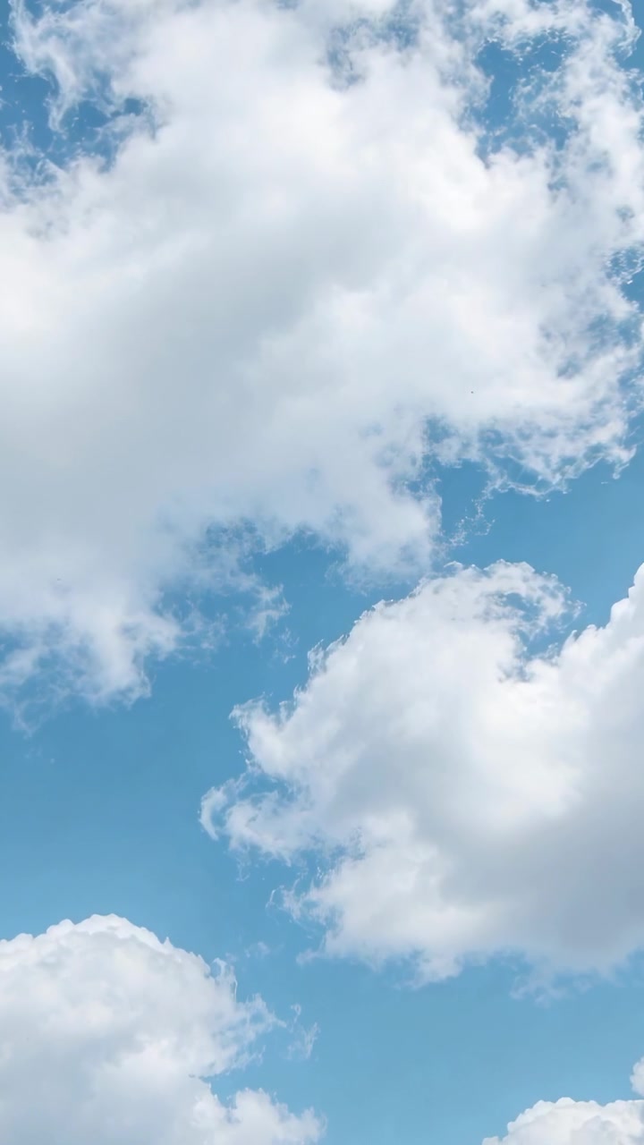 Video verticale: Grandi nuvole cumulo bianche alla deriva che cambiano forma nel cielo blu diurno, mosse dal vento