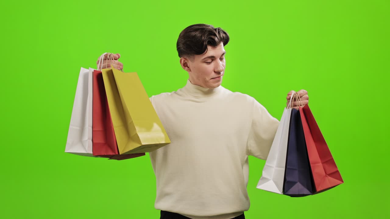 남자는 서서 쇼핑백을 들고 카메라를 바라보고 미소 짓고 초록색 바탕에 서 있습니다.