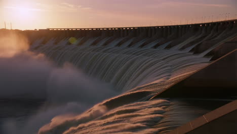 dramatic sunset over a large dam with water flowing from spillways