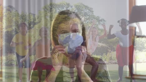 Caucasian-woman-wearing-a-face-mask-against-group-of-diverse-kids-jumping-together-in-the-garden