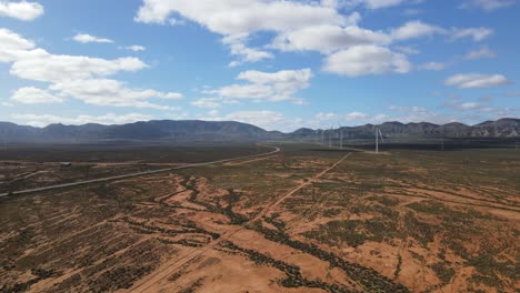 antena de drones moviéndose hacia un parque eólico en el país australiano con montañas en el fondo y un pájaro volando cerca el día de verano