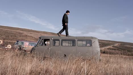 man standing on car in grassy valley