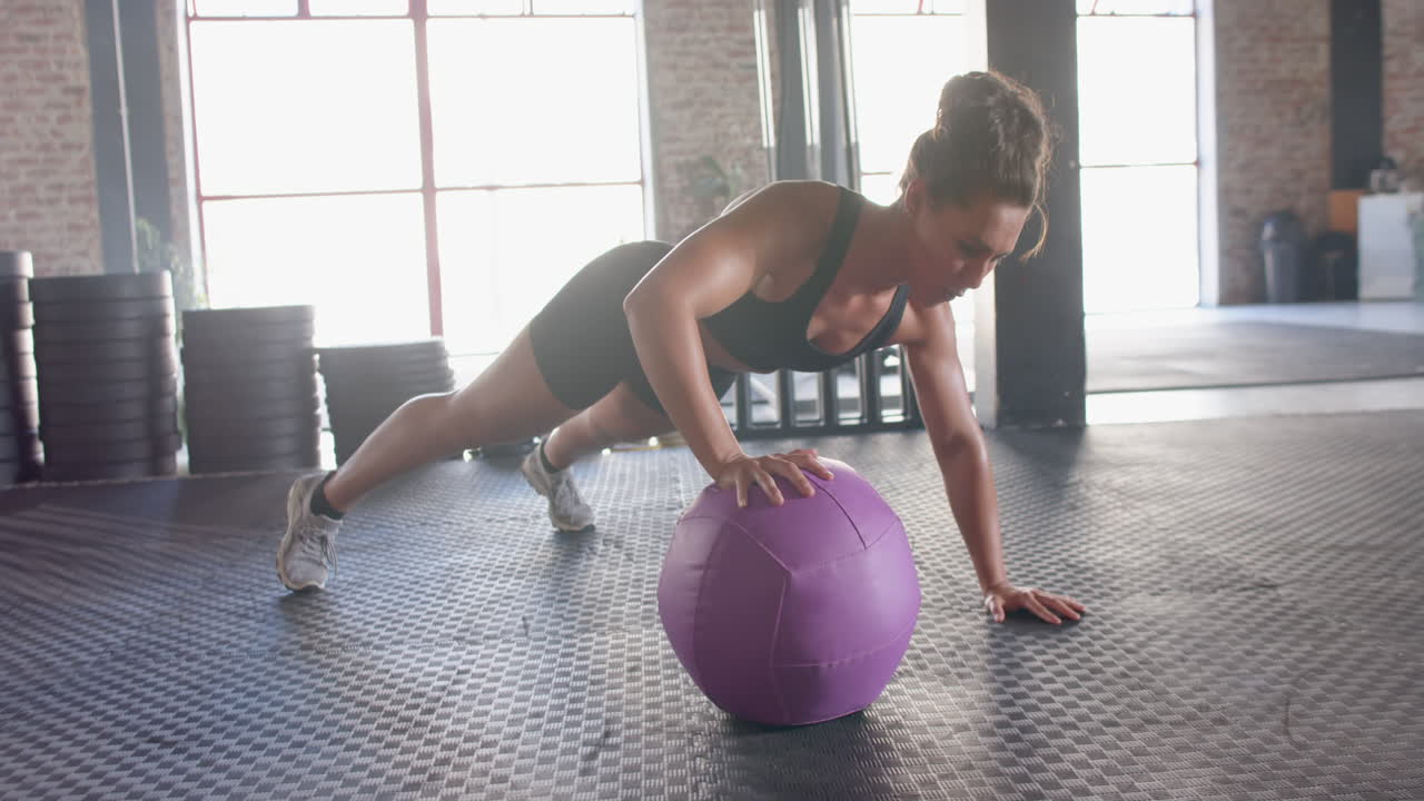 Exercising in gym, woman doing push-ups with purple medicine ball