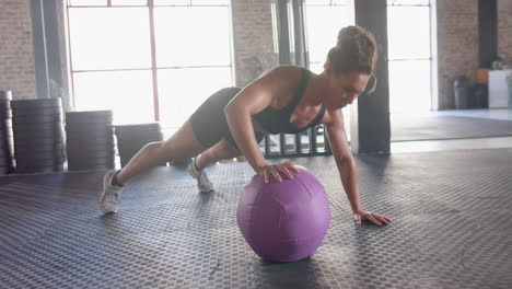 exercising in gym, woman doing push-ups with purple medicine ball