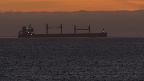 big ship sailing in the sea at sunset with small boat leaving faster