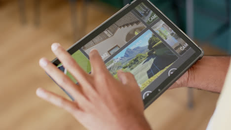 hands of biracial man using tablet with home security camera views on screen, slow motion