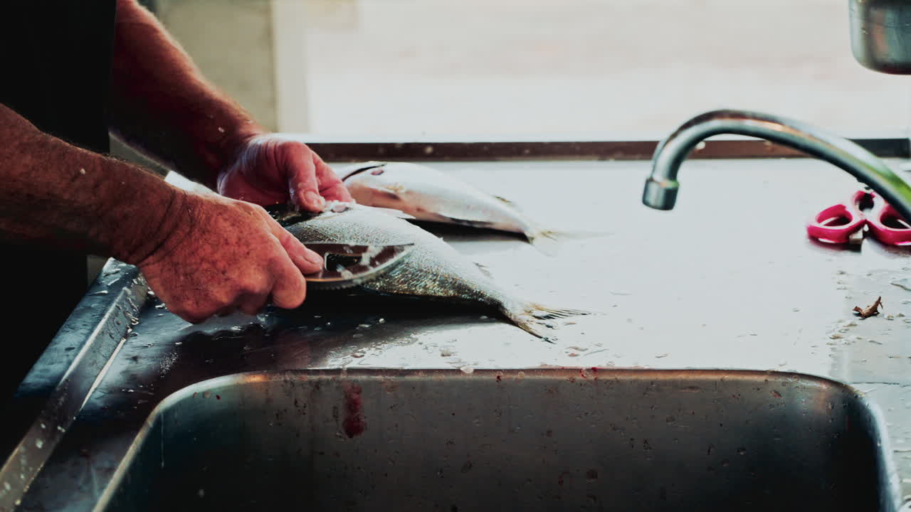 Hands of a fishmonger vigorously cleaning and scaling a fish at a stainless steel sink, water splashing around in a busy market preparation scene