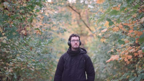 joven europeo con auriculares en un vibrante bosque mixto de otoño, observando las coloridas hojas de otoño