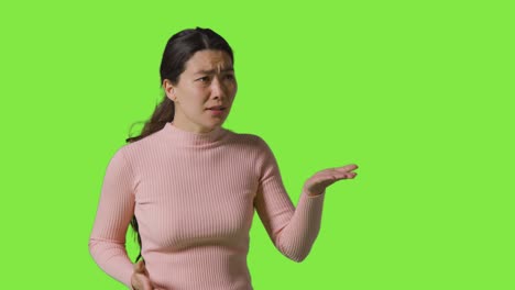 Studio-Portrait-Of-Frustrated-Angry-Woman-Standing-Against-Green-Screen-Shouting-At-Person-Off-Camera
