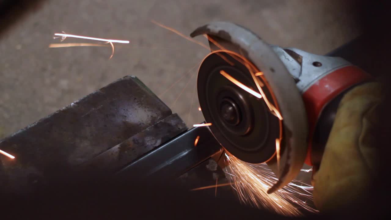 Close up of man using angle grinder to cut steel pipe, indoor handheld