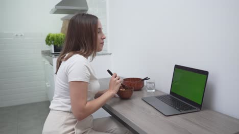 woman eating lunch at home while working on laptop