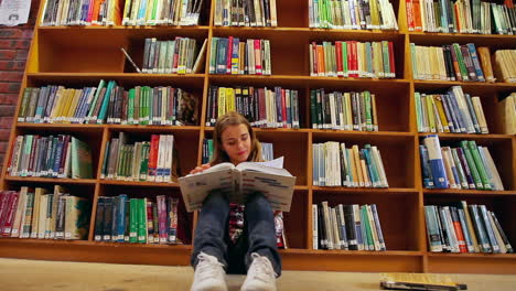 Hübsche-Studentin-Sitzt-Auf-Dem-Boden-Und-Liest-Ein-Buch-In-Der-Bibliothek