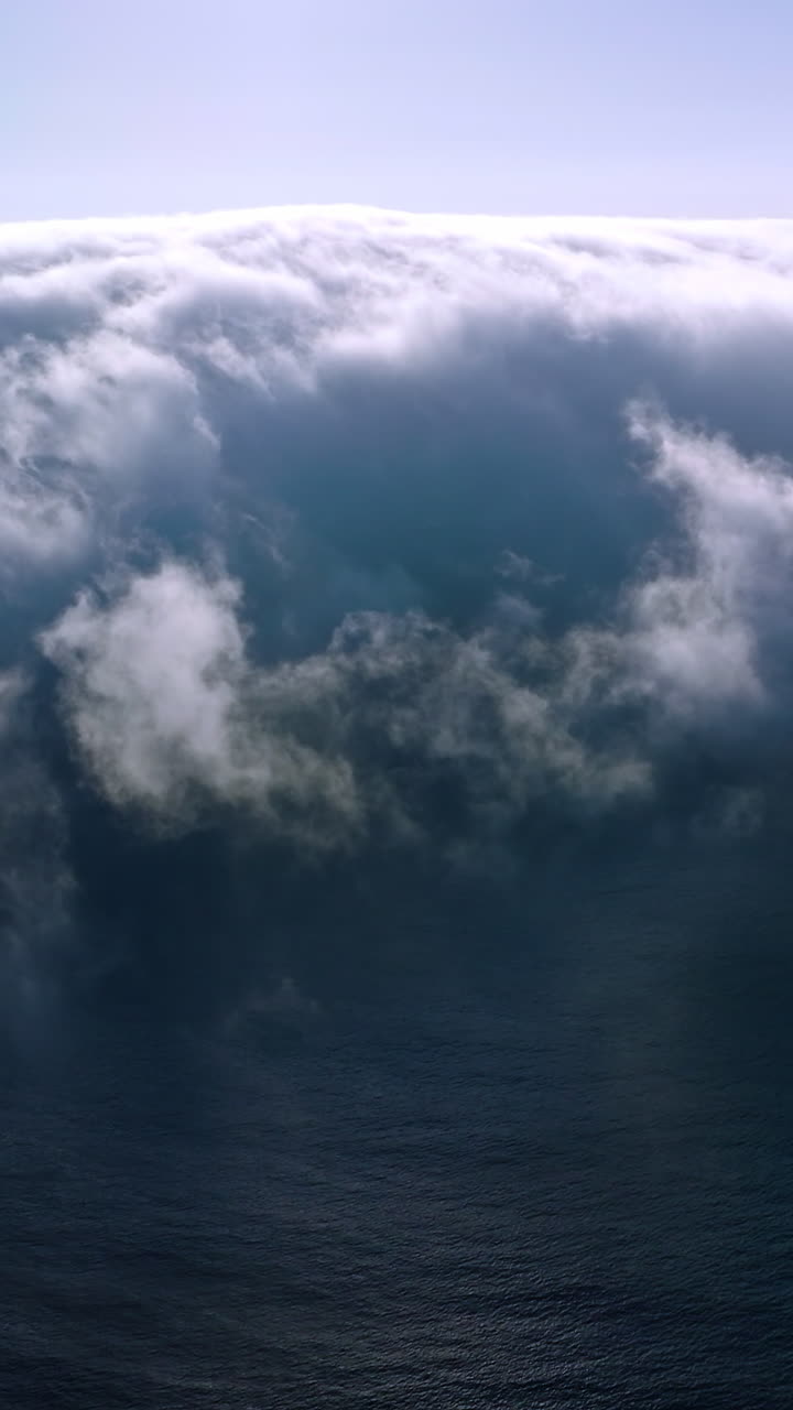 Blue ocean water covering with thick fog. Bright sun shining on the top of hazy cloudscape. Aerial view. Vertical video