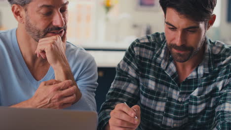 pareja masculina del mismo sexo que usa una computadora portátil en casa para verificar las finanzas domésticas