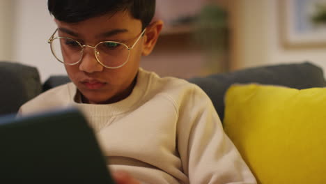 close up of young boy sitting on sofa at home playing games or streaming onto digital tablet 8