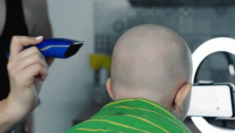 mother cutting the hair of a little son with a hair clipper on the kitchen.