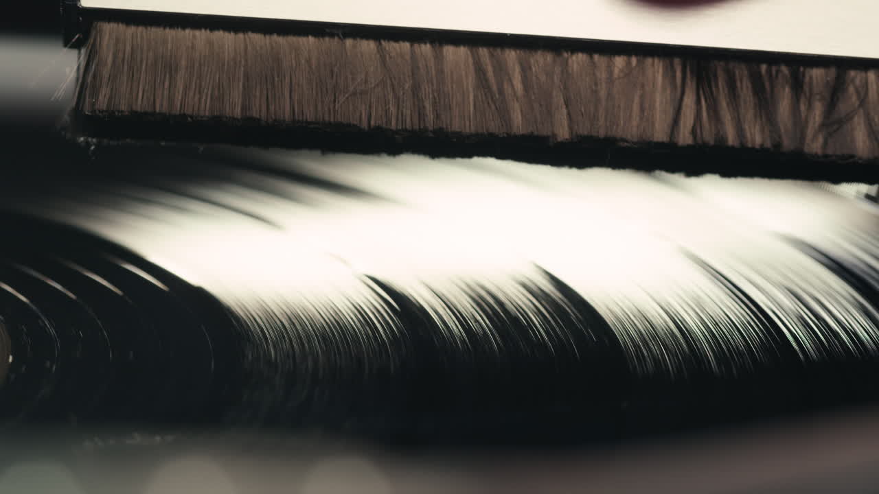 Nærbillede af en hånd, der renser en roterende vinylplade med en børste