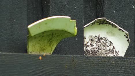 View-of-vintage-old-colorful-ceramic-dish-fragments-placed-on-a-black-painted-wooden-wall,-closeup-slow-zoom-in-shot