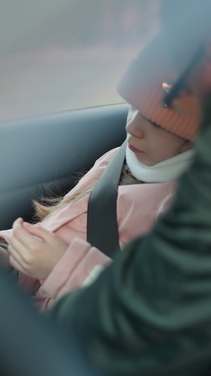 초록색 재을 입은 남자가 차 안에 분홍색 자켓을 입은 어린 딸의 안전벨트를 벗고 있는 것을 볼 수 있습니다.