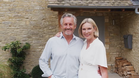 Portrait-Of-Loving-Senior-Couple-Standing-Outside-Front-Door-Of-Home