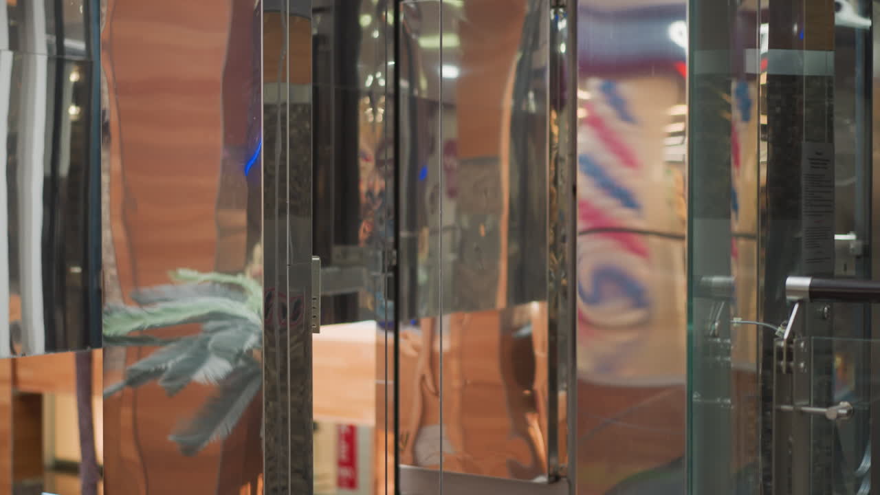 현대적인 쇼핑몰에서 내려오는 우아한 유리 엘리베이터, 활기찬 반사, 상세한 기계 구조, 그리고 내부 조명의 흐릿한 배경, 현대적인 디자인을 혼합합니다.