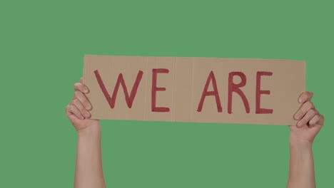 hands hold a poster with the slogan we are against the background of a green screen, chroma key. stop racism concept, no racism. close up. slow motion