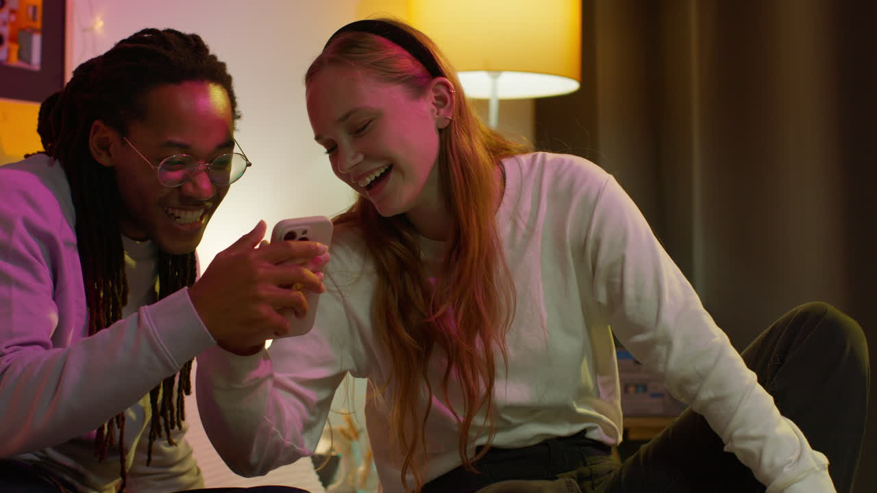 una pareja joven riendo juntos mientras miran un teléfono