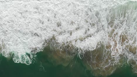 Top-down-slow-aerial-shot-following-the-ocean-waves-as-they-crash-on-the-California-shore-near-Montara