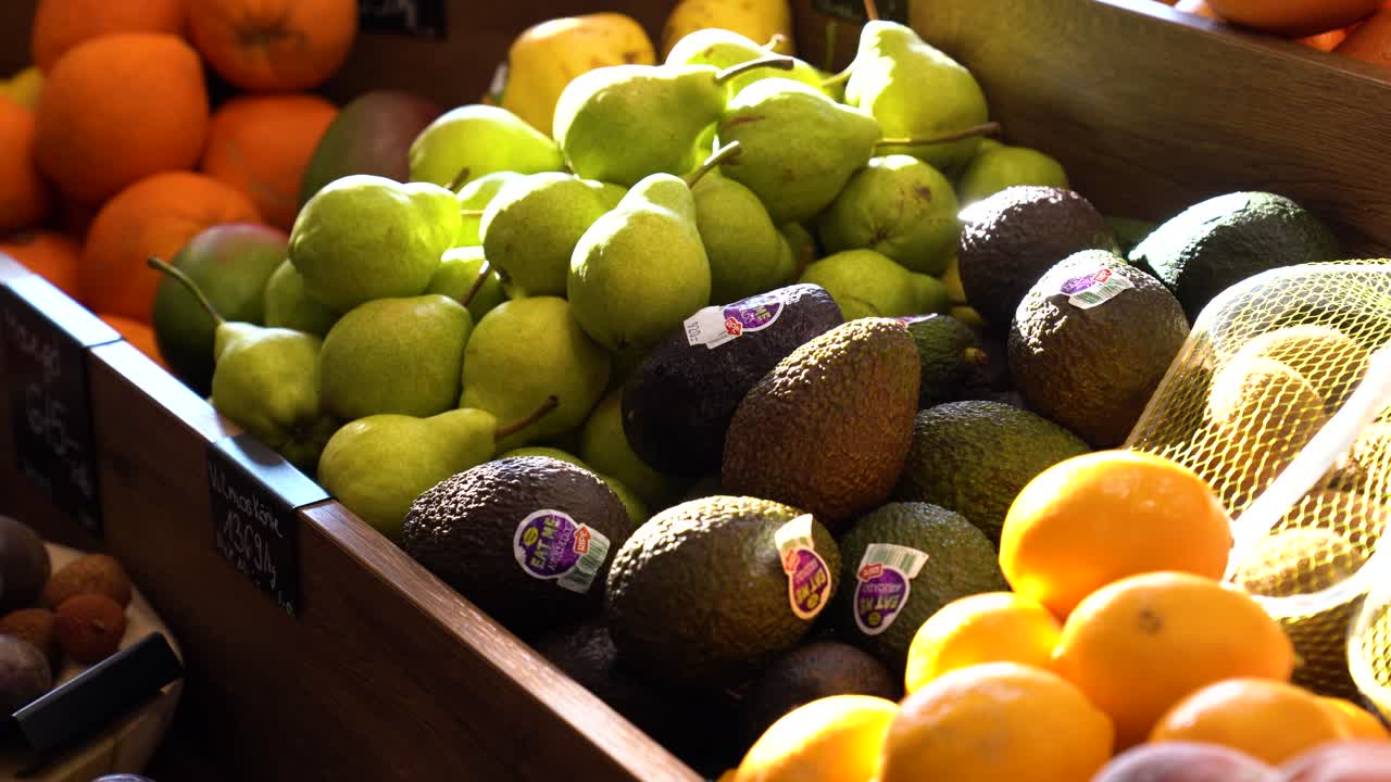 Display of pears, avocados, other fruit for sale in market lit by morning light slow left to right pan