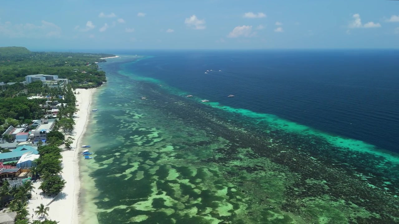 Il drone si allontana e sale sopra Alona Beach, rivelando sabbia bianca, acque basse della barriera corallina, la costa e il mare blu profondo a Panglao, Bohol