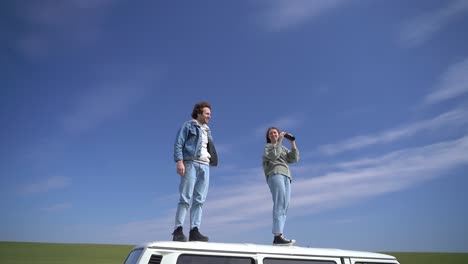 a young boy and young girl look around with a pair of binoculars on the roof of a caravan.